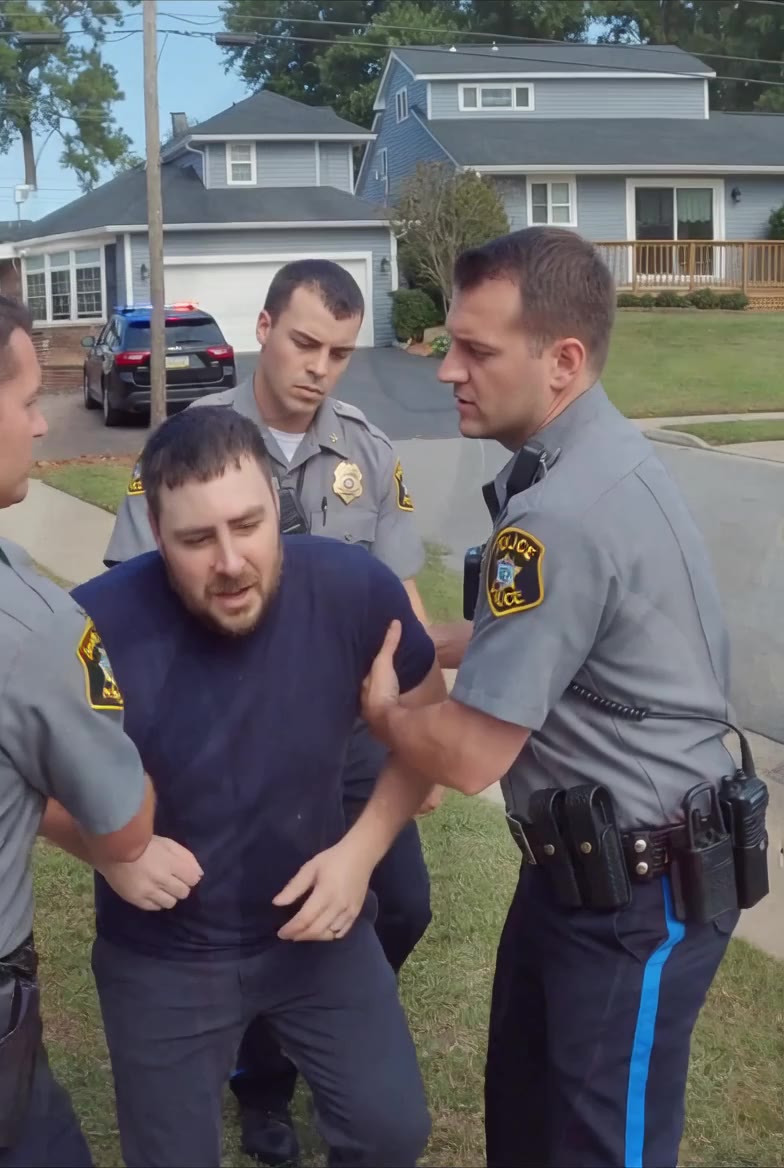 Officers holding Scott Lafferty by both arms on a residential lawn during an arrest for filing a false report.