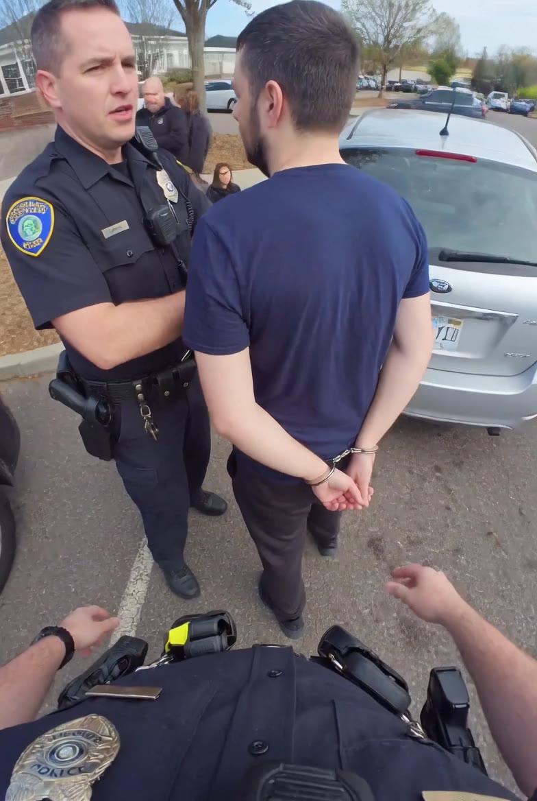 Scott Lafferty in a navy shirt, hands cuffed behind his back, standing with an officer in a Stop & Shop parking lot.